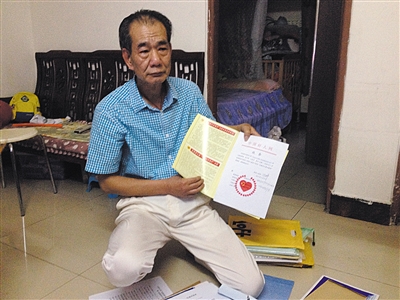 翻出一家網(wǎng)站贈(zèng)予的“中國好人”證書，區(qū)少坤單膝跪在地上，“你看，我是中國好人啊。” 范春旭 攝