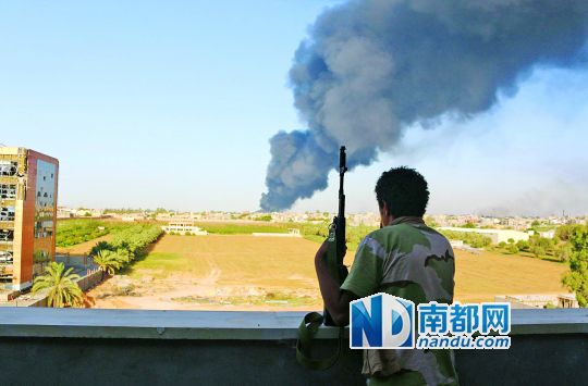 2日，利比亞首都的黎波里，一民兵武裝成員眺望被火箭彈擊中的儲(chǔ)油罐冒出濃煙。