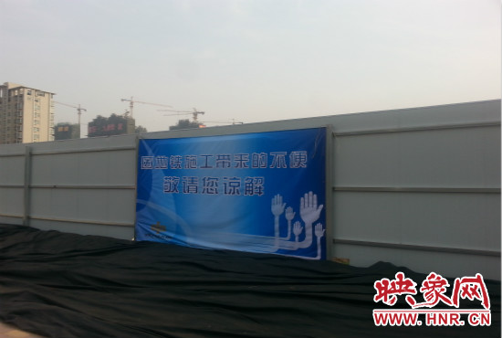 道路南側(cè)圍起了白色的圍擋，墻上標示著“因地鐵施工帶來的不便敬請您諒解”的提示牌。