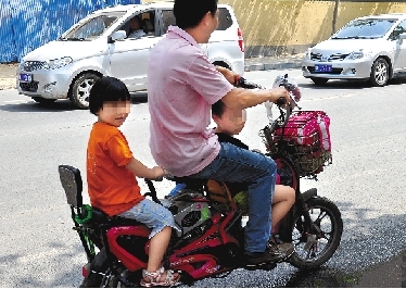 周先生騎著一輛低矮的電動車帶著一對兒女，很不安全。