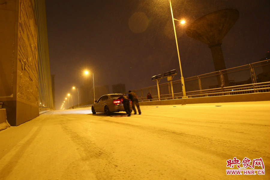 雪天路滑，汽車上橋打滑，兩名“推車人”幫助一輛私家車上坡。