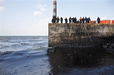 昨日，山東青島，清污人員正在海邊清理油污。