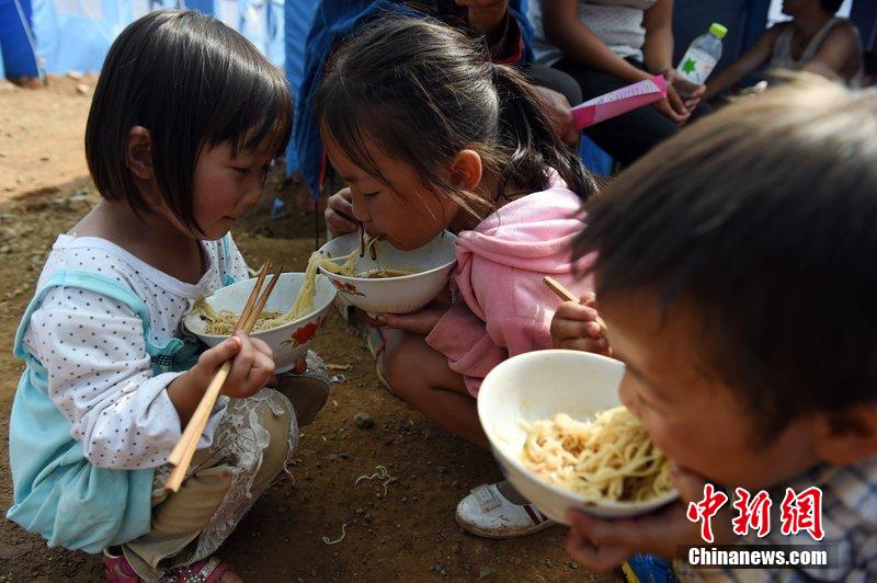 2014年8月6日，云南魯甸龍頭山災區(qū)，兒童在帳篷外吃飯。