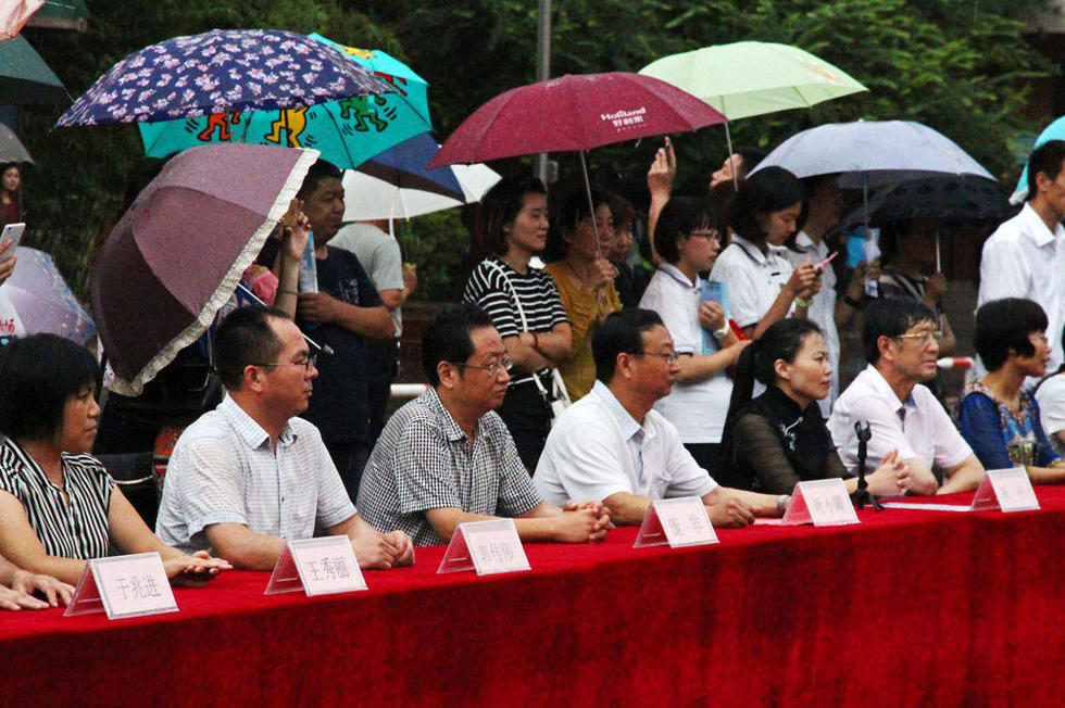 在主席臺上觀看的校領導也堅持不打傘陪學生一起淋雨，身旁站滿了打傘觀看的家長。