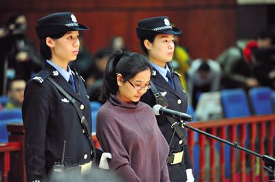 被告人盧梅低著頭，站在朝陽(yáng)法院刑事審判庭的被告席上。